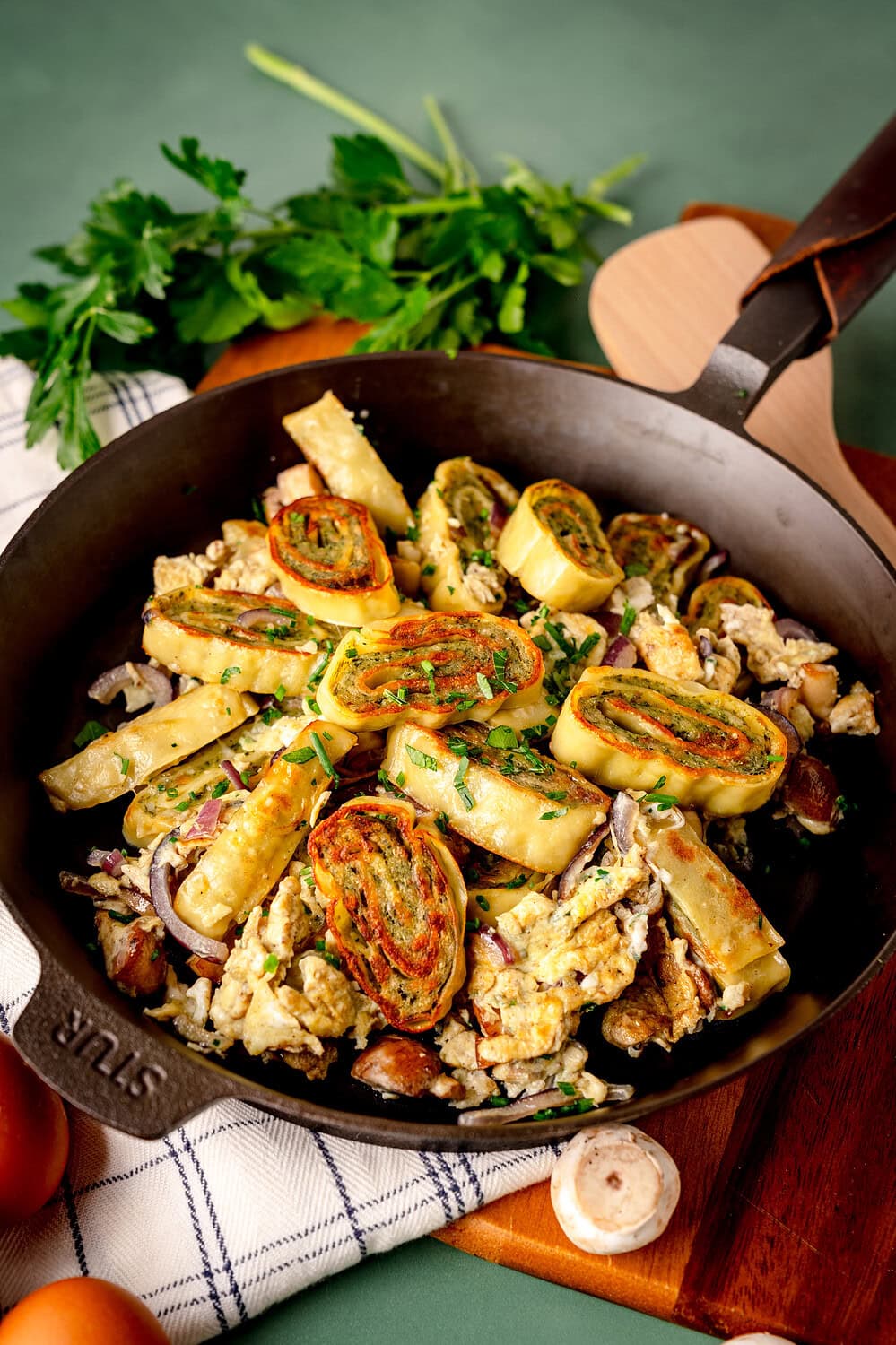 Quick Maultaschen pan in a cast iron pan with egg, onions and mushrooms as well as herbs. Served on a wooden board with a green background