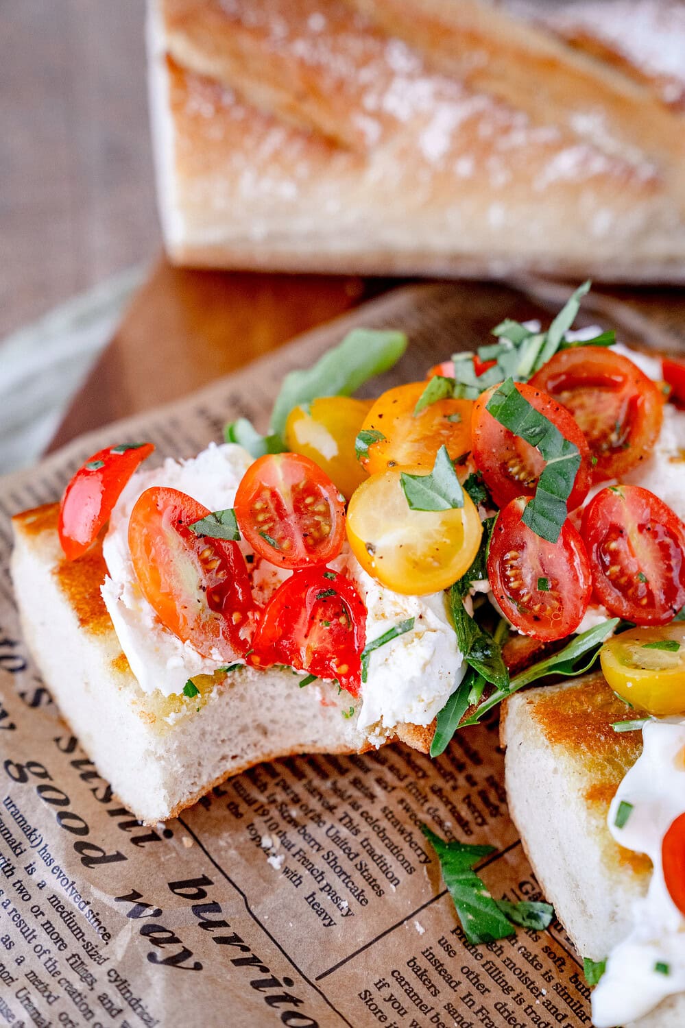 Toasted baguette with cherry tomatoes and burrata, a corner of which has already been bitten off.