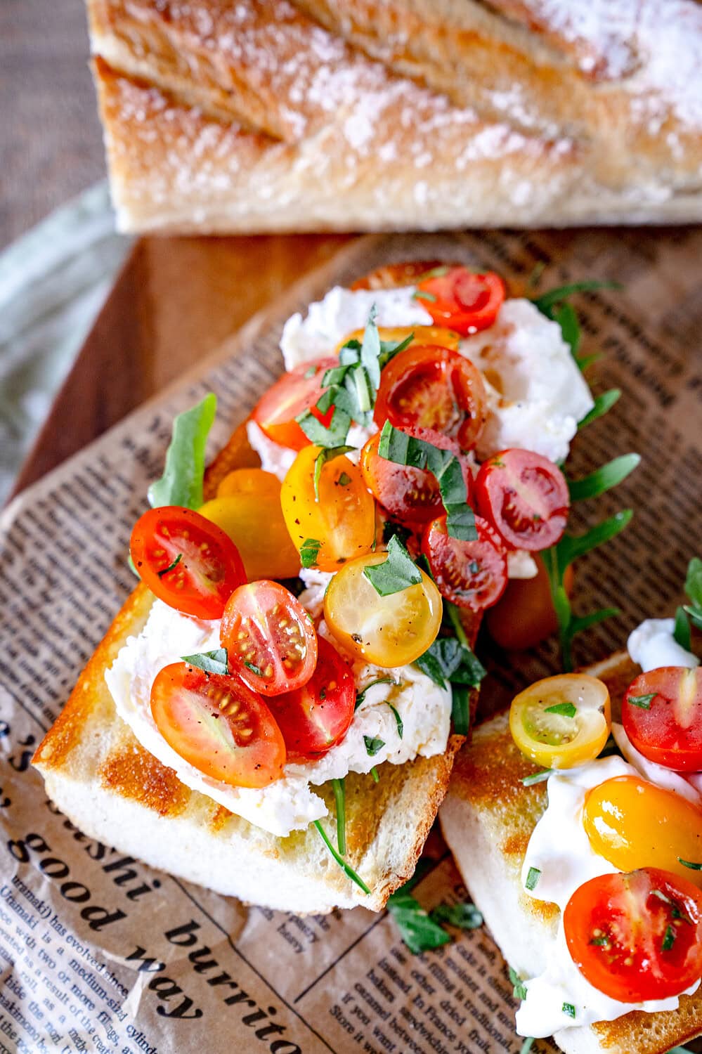 Burrata baguette with cherry tomatoes on a wooden board with wheat baguette in the background