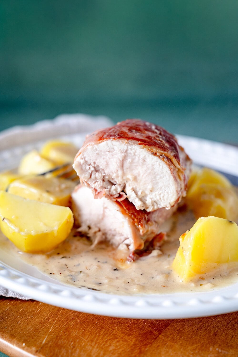 Sliced chicken breast wrapped in bacon on potatoes and with a parmesan sauce