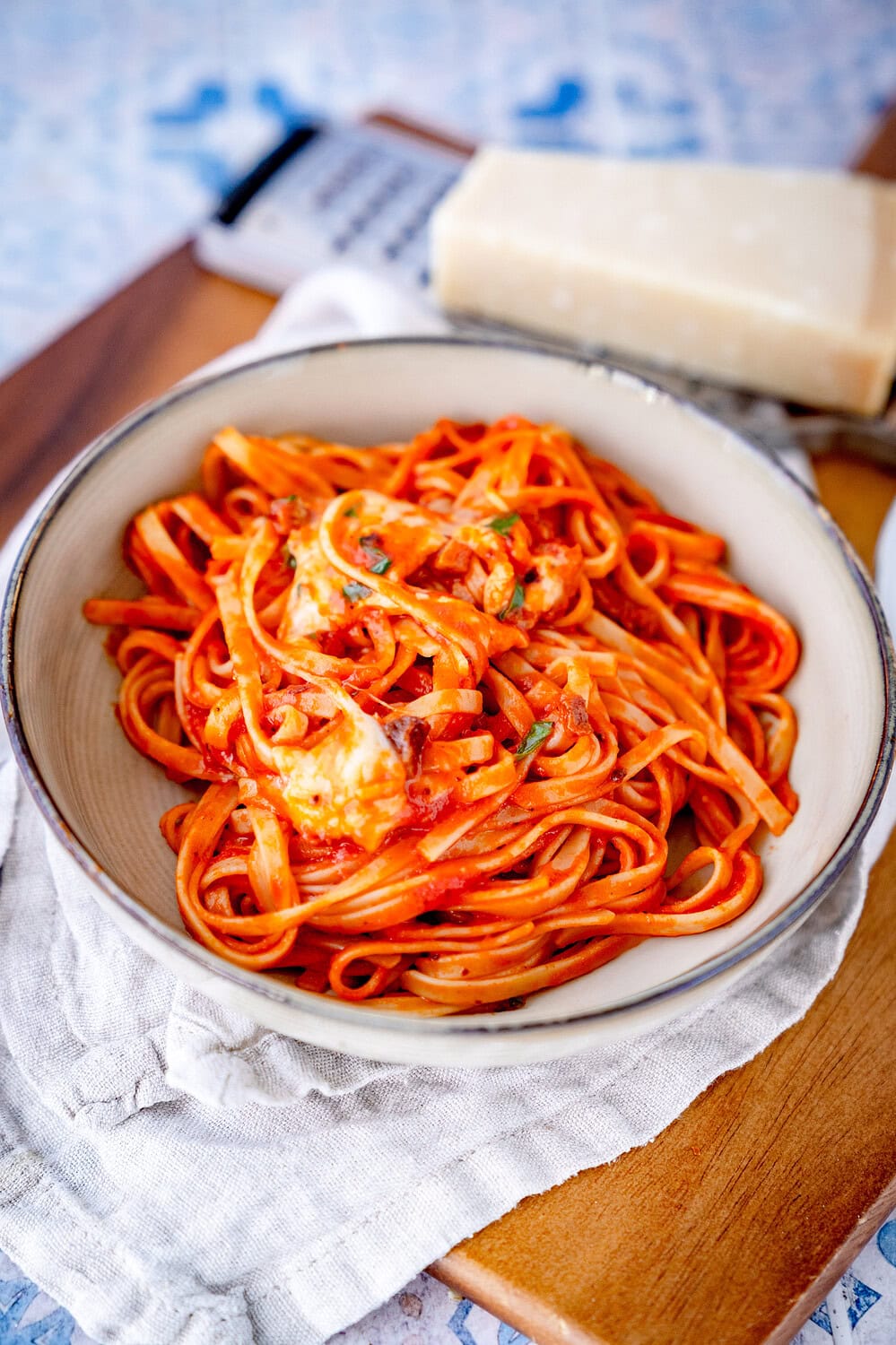 Creamy linguine with guanciale and mozzarella on a deep plate on a wooden board with a piece of parmesan on a grater in the background