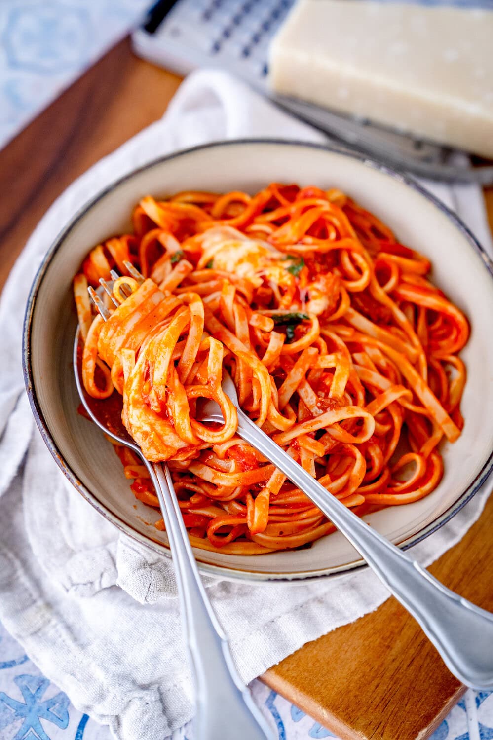 Creamy linguine with mozzarella and guanciale wrapped around a fork and spoon in a deep plate on a wooden board.