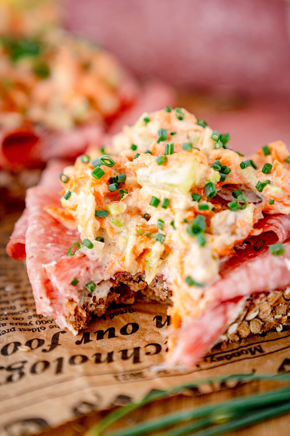 A bitten smörrebröd with Aoste Le Briedu salami and a topping of carrots, apples and chives