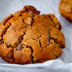 Ein Nutella Cookie aus der Heißluftfritteuse und ein weiterer Cookie, soweie Schokoriegel im Anschnitt auf einem weißen Backpapier