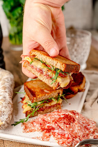 Angeschnittenes Croque Aoste in der Hand gehalten und hauchdünne Aoste Ringsalami