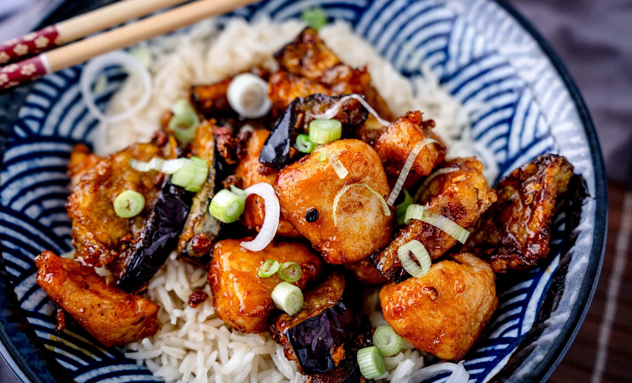 Asiatisch frittierte Auberginen mit Hähnchenfleisch und Reis in einer Schale mit Essstäbchen von schräg oben im Querformat