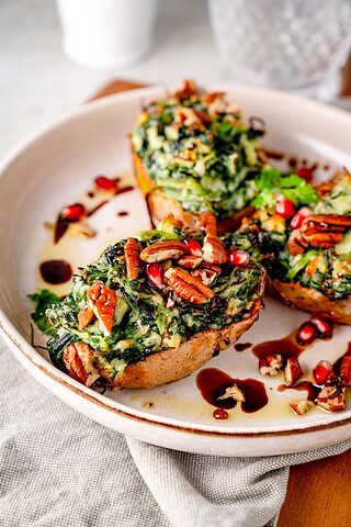 Gebackene Ofenkartoffeln mit, Nüssen und Granatapfelkernen auf einen weißen Teller.