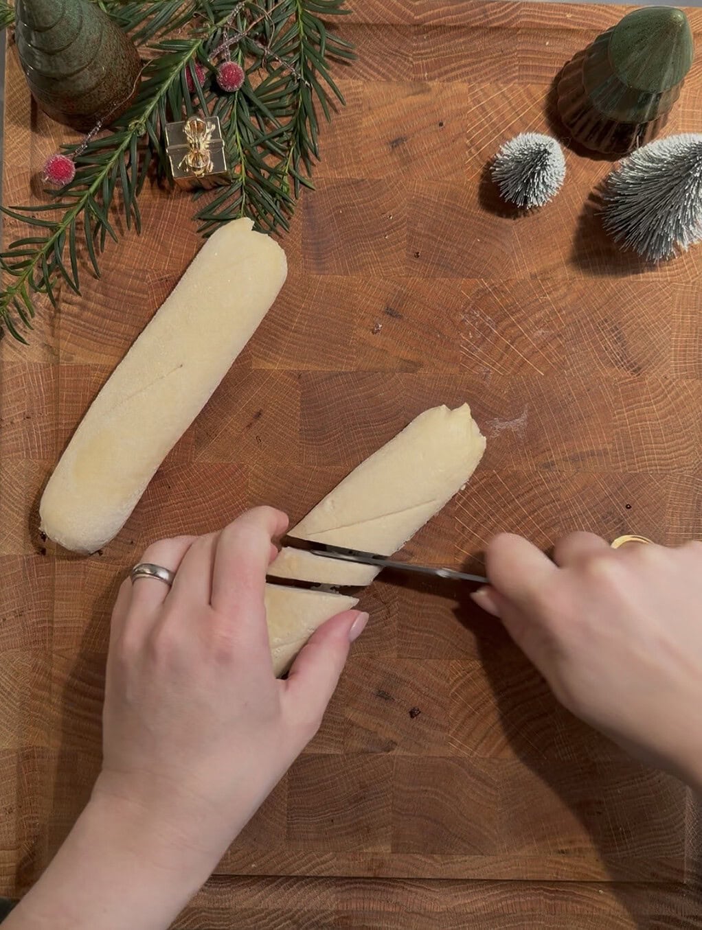 Schneid-Vorgang von Käse auf einem Holzbrett mit Weihnachtsdeko im Hintergrund.