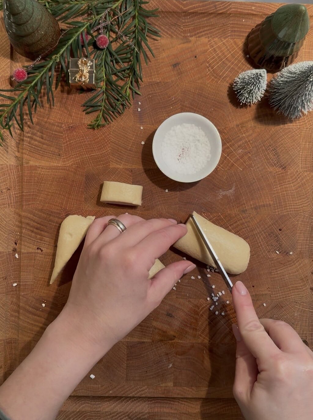 Blätter und Tannenzapfen auf Holz, Person schneidet Teig in Stücke.