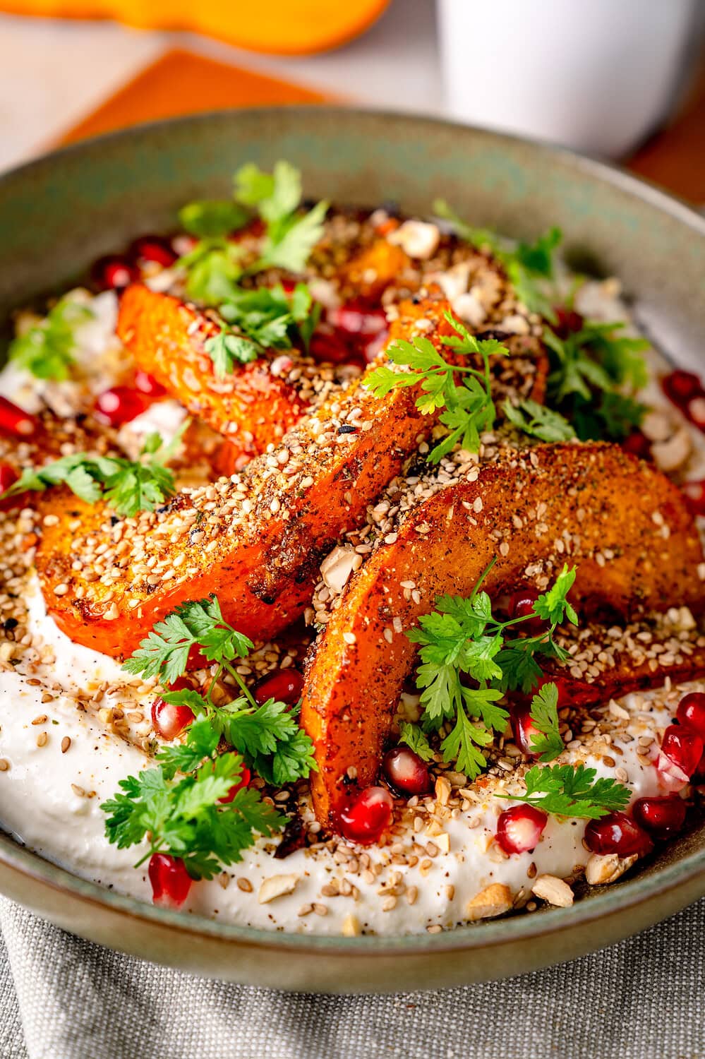 Gebratene Kürbisscheiben mit Granatapfel, Joghurt und Nüssen auf einem Teller.