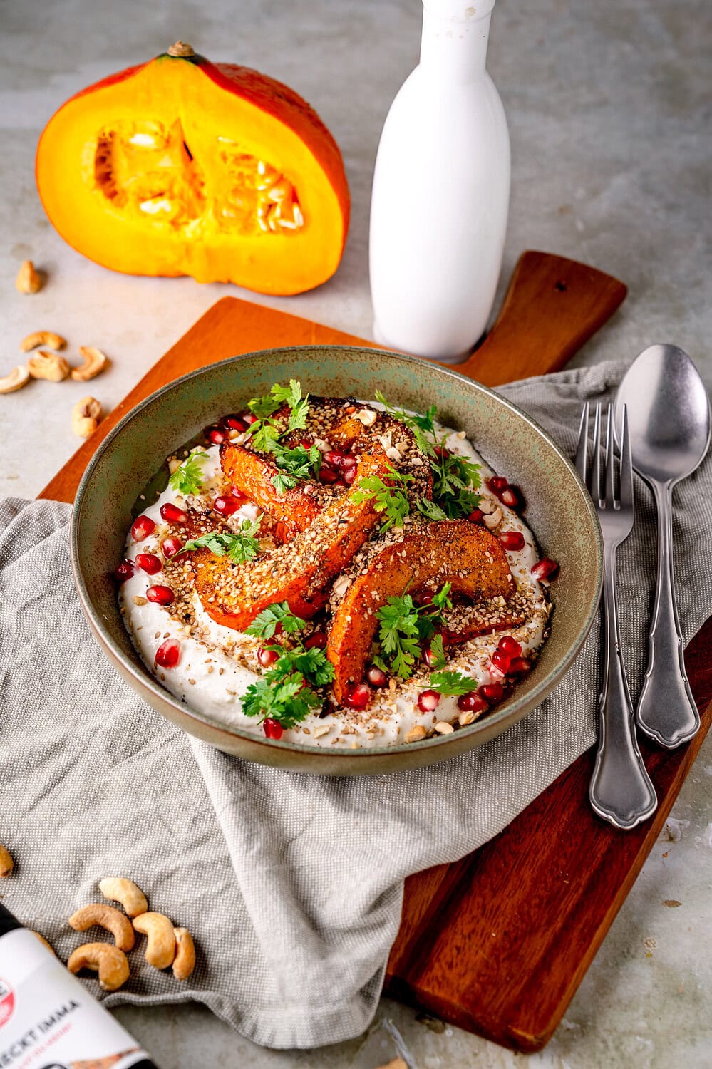 Gebratene Kürbisspalten auf cremigem Joghurt mit Granatapfelkernen und Kräutern.