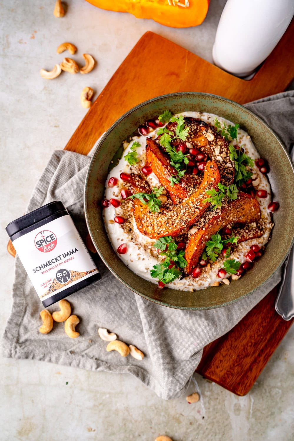 Geröstete Kürbisfilets mit Tahini-Sauce und Granatapfelkernen auf einem Teller.