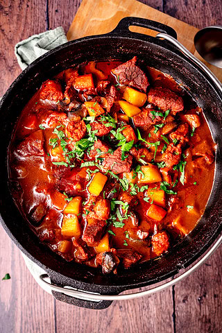 Herzhaftes Rindergulasch in einem Schmortopf mit Gemüse und frischer Petersilie.