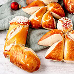 Frische Weihnachtsbrötchen auf weissem Holz mit festlicher Dekoration, traditionelles Gebäck. Laugengebäck Weihnachten Lausebengel Nikolausstiefel