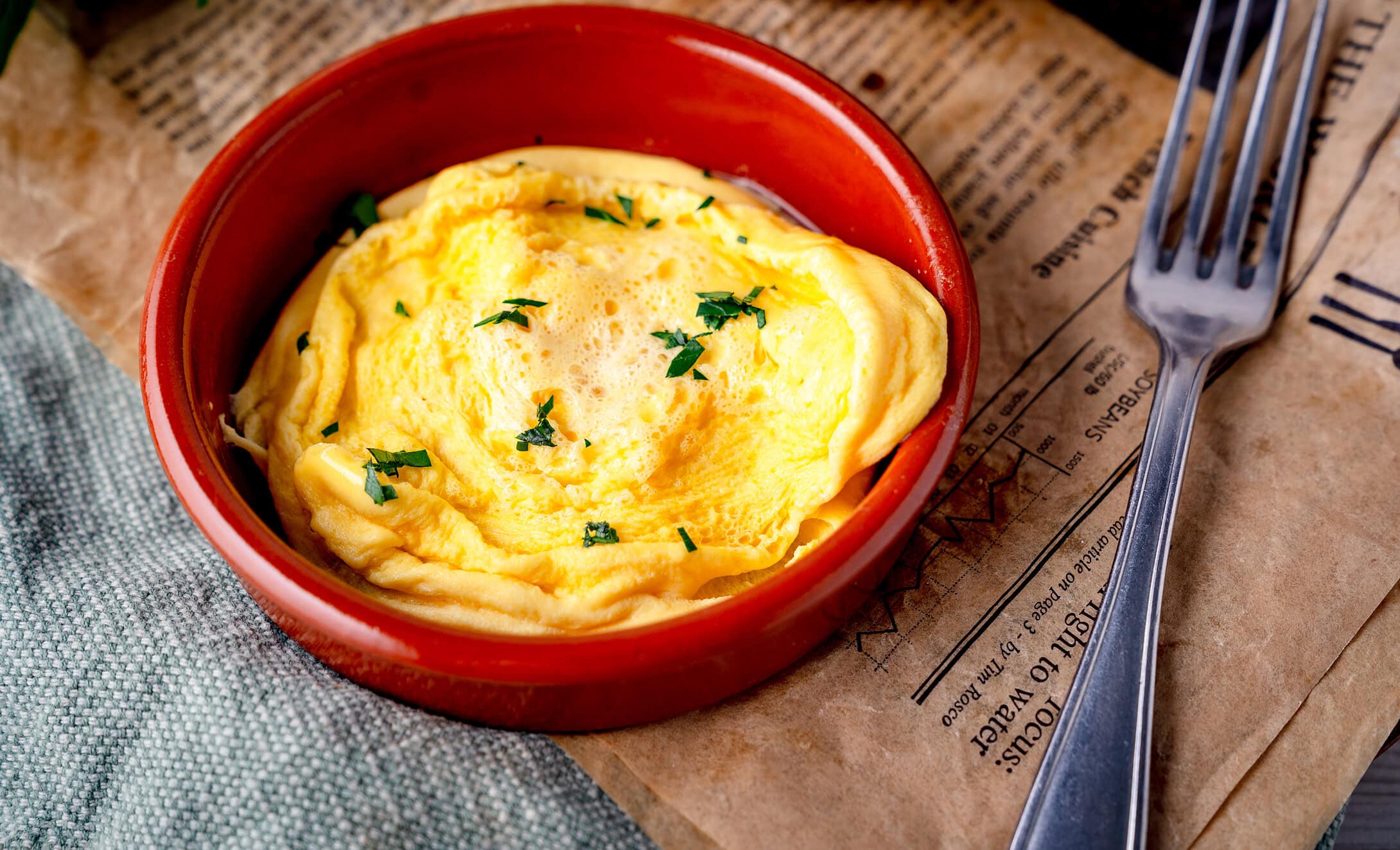 Fluffiges Omelett in roter Form mit frischen Kräutern auf Papier Untergrund.