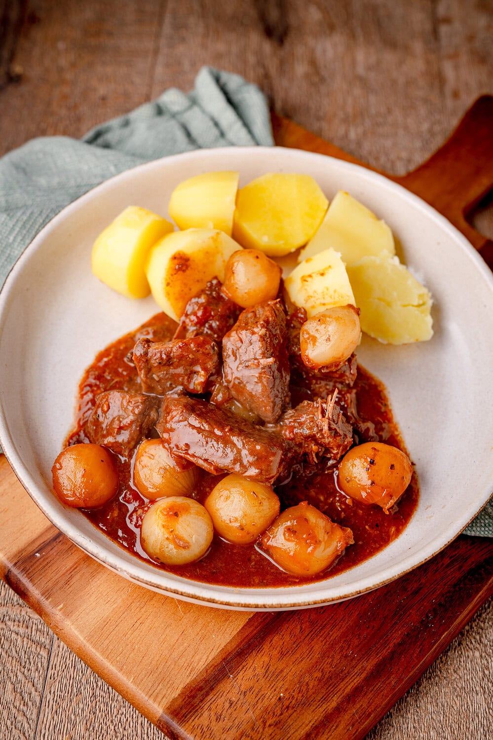 Stifado mit Perlzwiebeln auf einem tiefen Teller mit Salzkartoffeln.