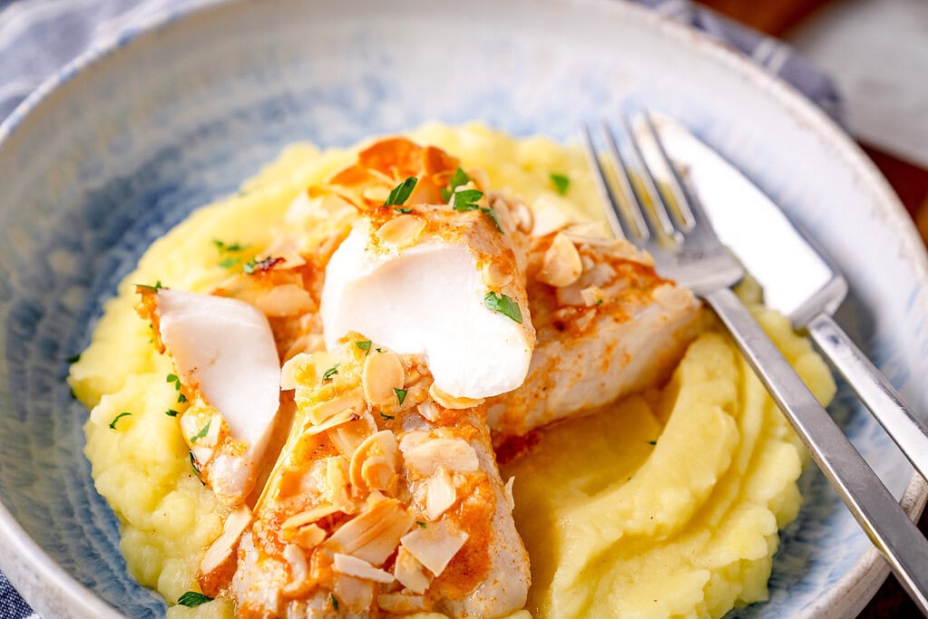 Hähnchen auf cremigem Kartoffelpüree, garniert mit Nüssen und frischen Kräutern, servierfertig.