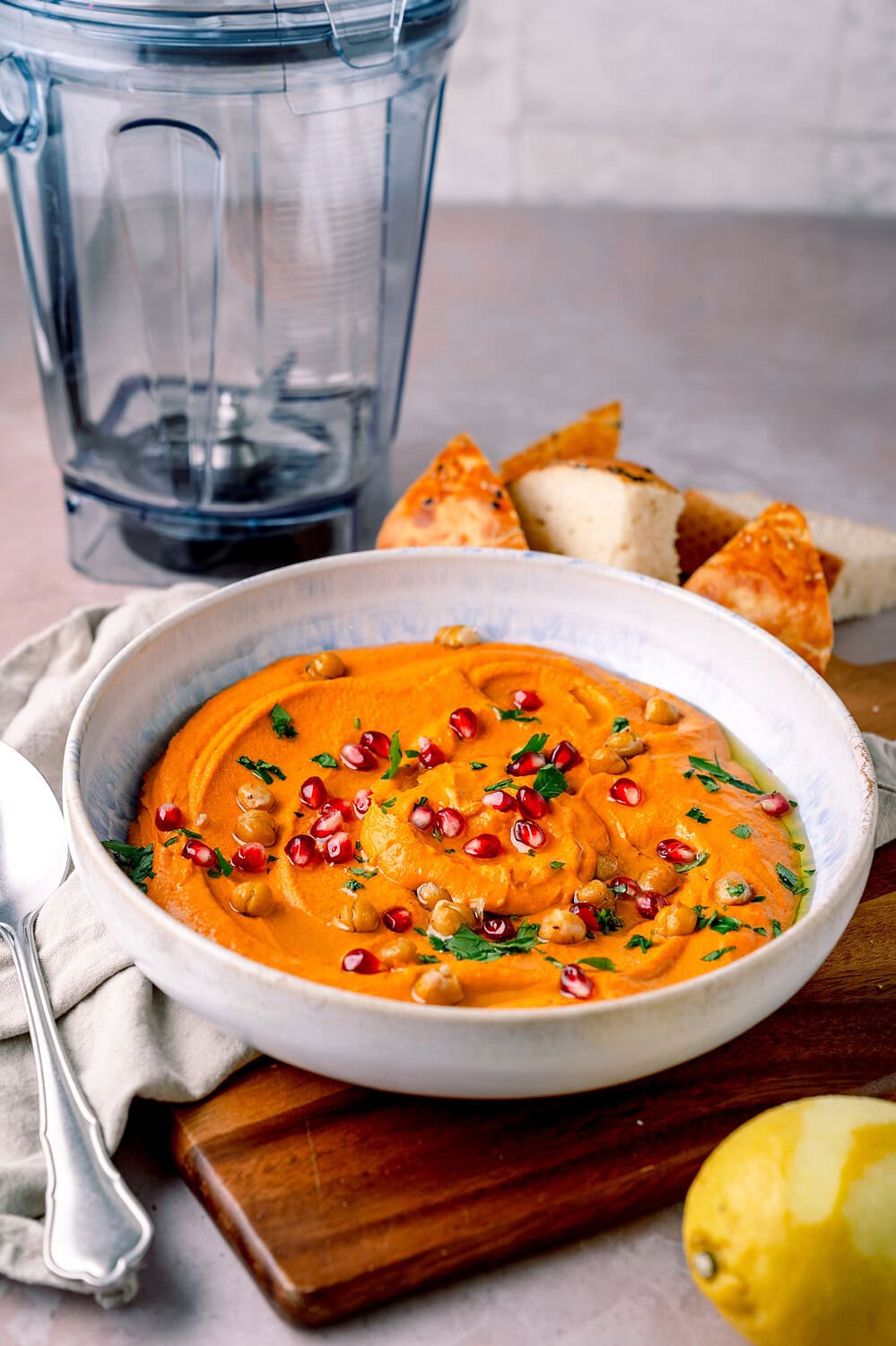 Leckeres PaprikaHummus mit Tomaten, Granatapfel, Kräutern und Sesamöl in einer Schüssel.