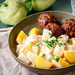 Rahm Kohlrabi mit Salzkartoffeln und Frikadellen auf einem grünen Teller auf grünem Untergrund.