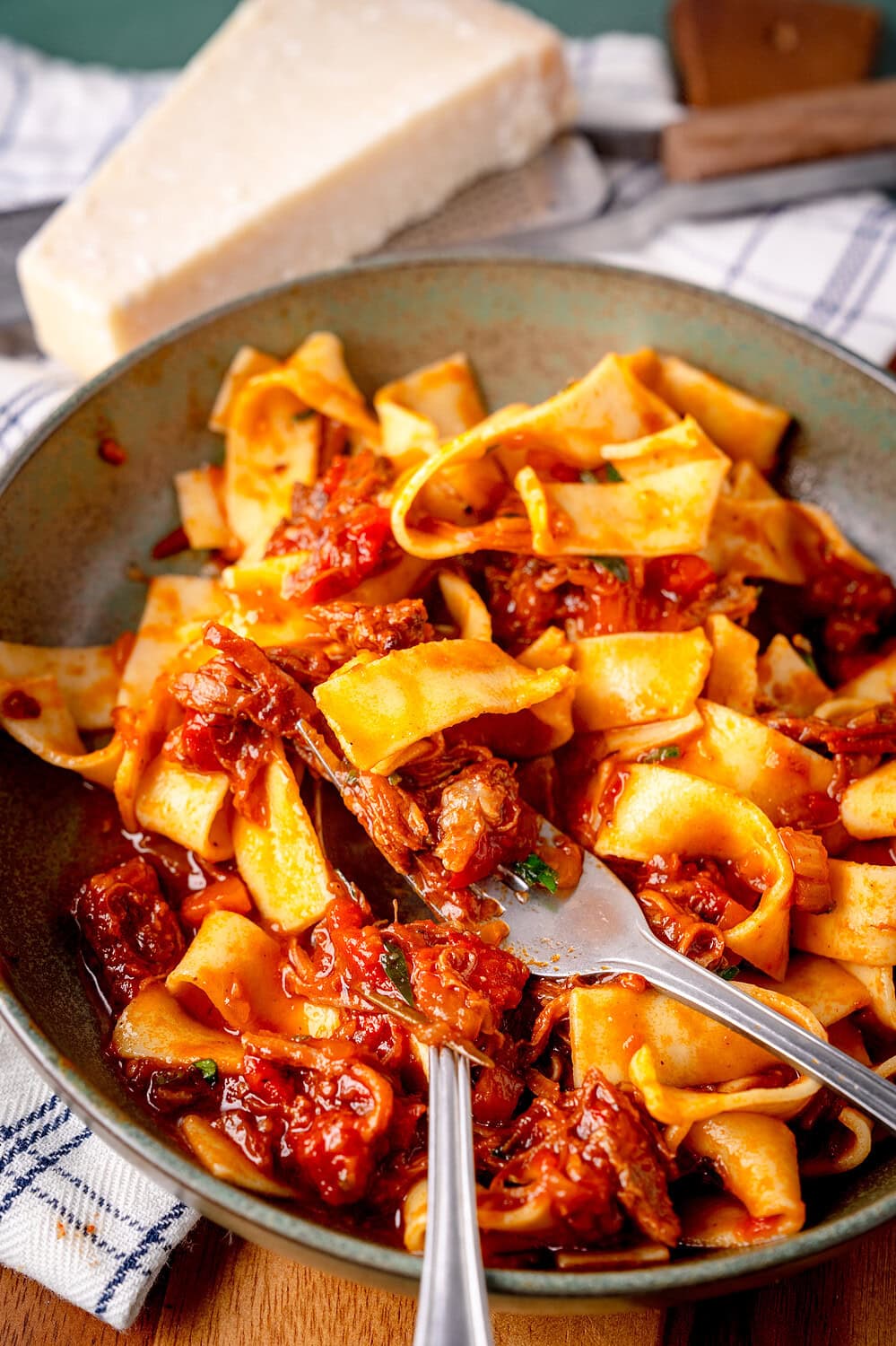 Bolognese mit Short Ribs mit Nudeln zusammen auf einem grünen Teller mit Gabel und Löffel