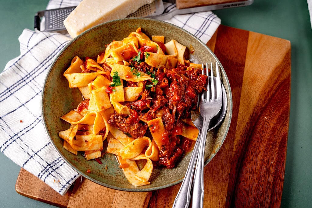 Bolognese aus Schmorfleisch auf einem tiefen Teller mit grünem Hintergrund