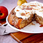 Gestürzter Apfelkuchen mit Walnüssen und Sahne sowie Gewürzsud auf weißem Teller mit Äpfeln