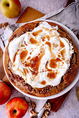 Gestürzter Apfelkuchen mit Walnüssen und Sahne sowie Gewürzsud auf weißem Teller mit Äpfeln
