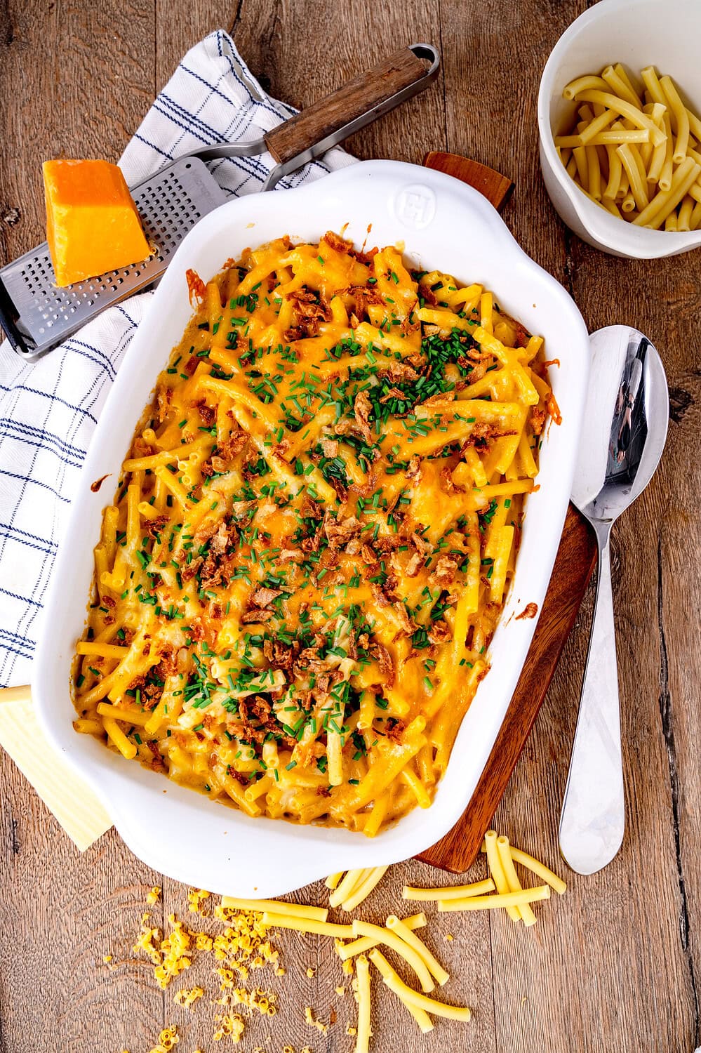 Mac and Cheese in einer Auflaufform auf einem Brett und einer Käsereibe mit Bergkäse