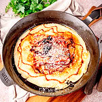 Frische Speckpfannkuchen in einer Pfanne mit frischen Kräutern im Hintergrund.