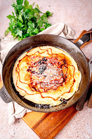 Frische Speckpfannkuchen in einer Pfanne mit frischen Kräutern im Hintergrund.