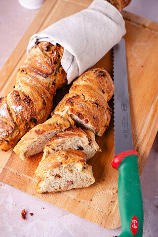 Frisches Zwiebel-Speck-Baguette, aufgeschnitten, auf Holzbrett, mit Brotmesser-Neuheit.