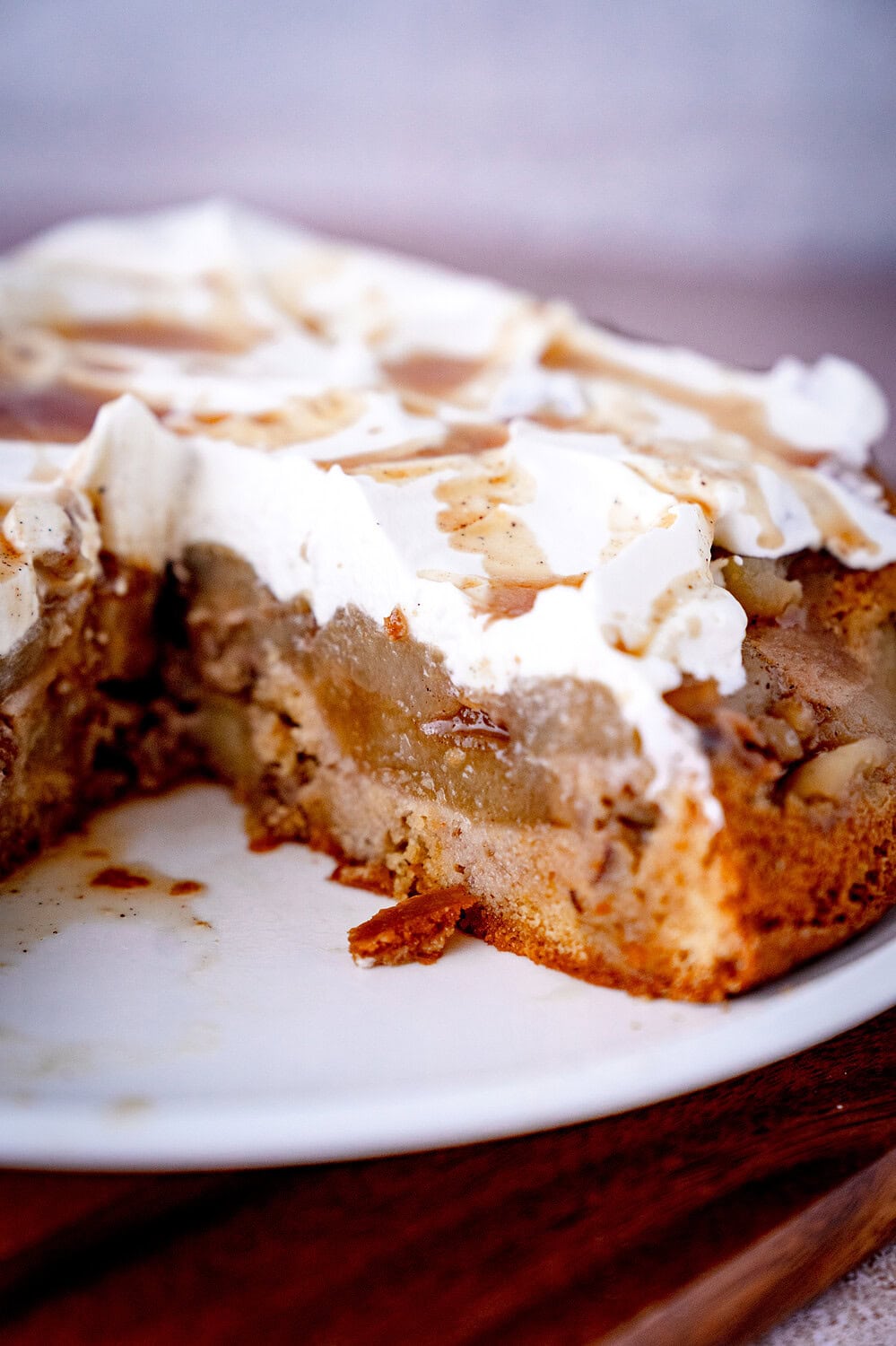 Gestürzter Apfelkuchen mit Walnüssen und Sahne sowie Gewürzsud auf weißem Teller mit Äpfeln