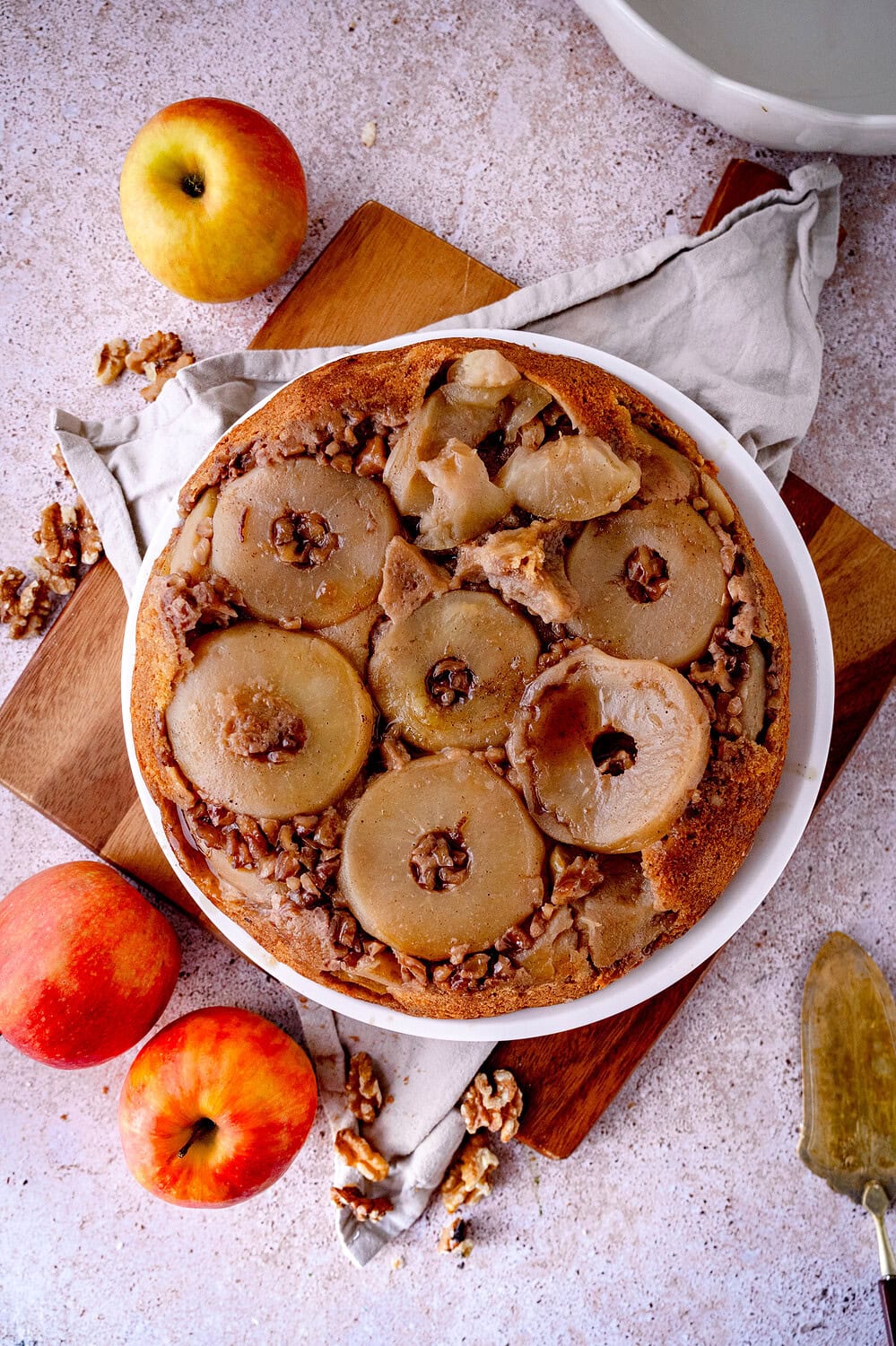 Gestürzter Apfelkuchen mit Walnüssen und Sahne sowie Gewürzsud auf weißem Teller mit Äpfeln