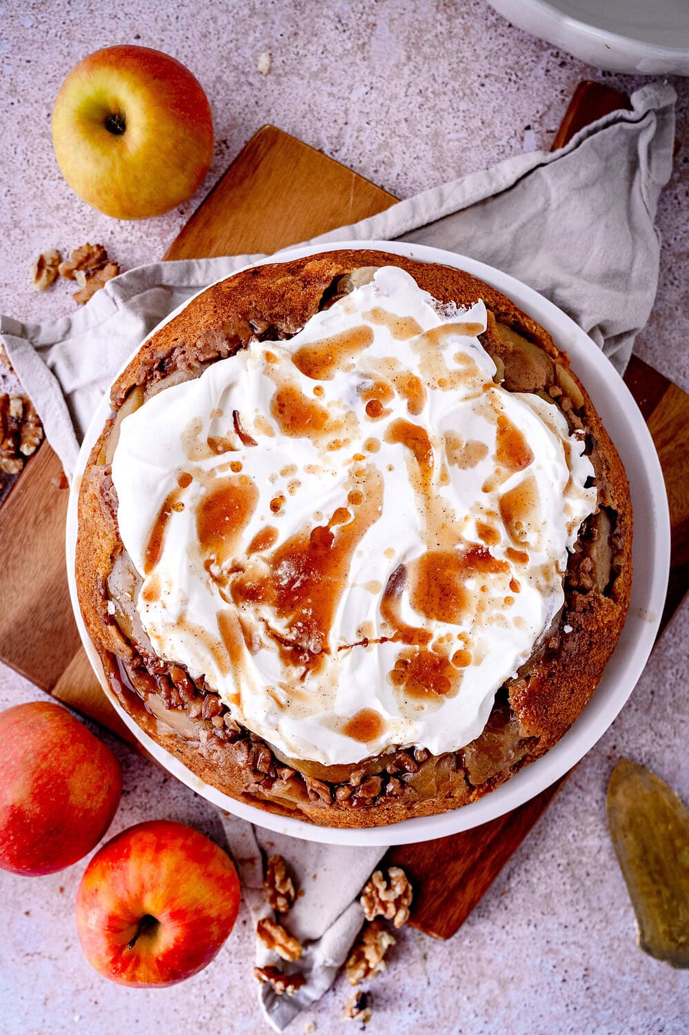 Gestürzter Apfelkuchen mit Walnüssen und Sahne sowie Gewürzsud auf weißem Teller mit Äpfeln
