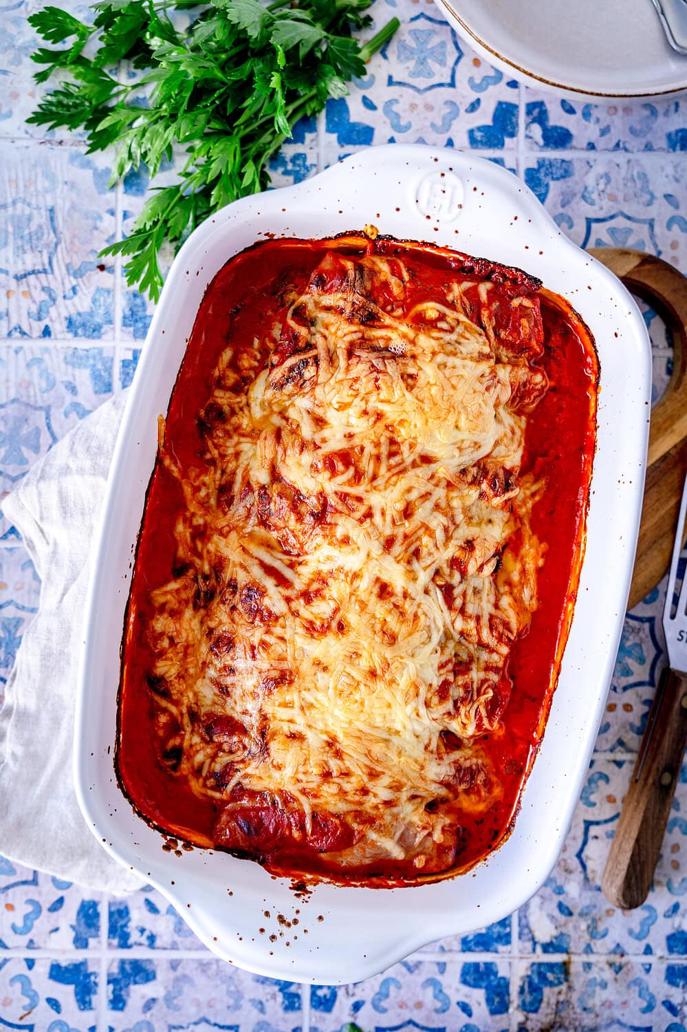 Ham and minced meat rolls gratinated with cheese and served with tomato sauce on a wooden board in a top view