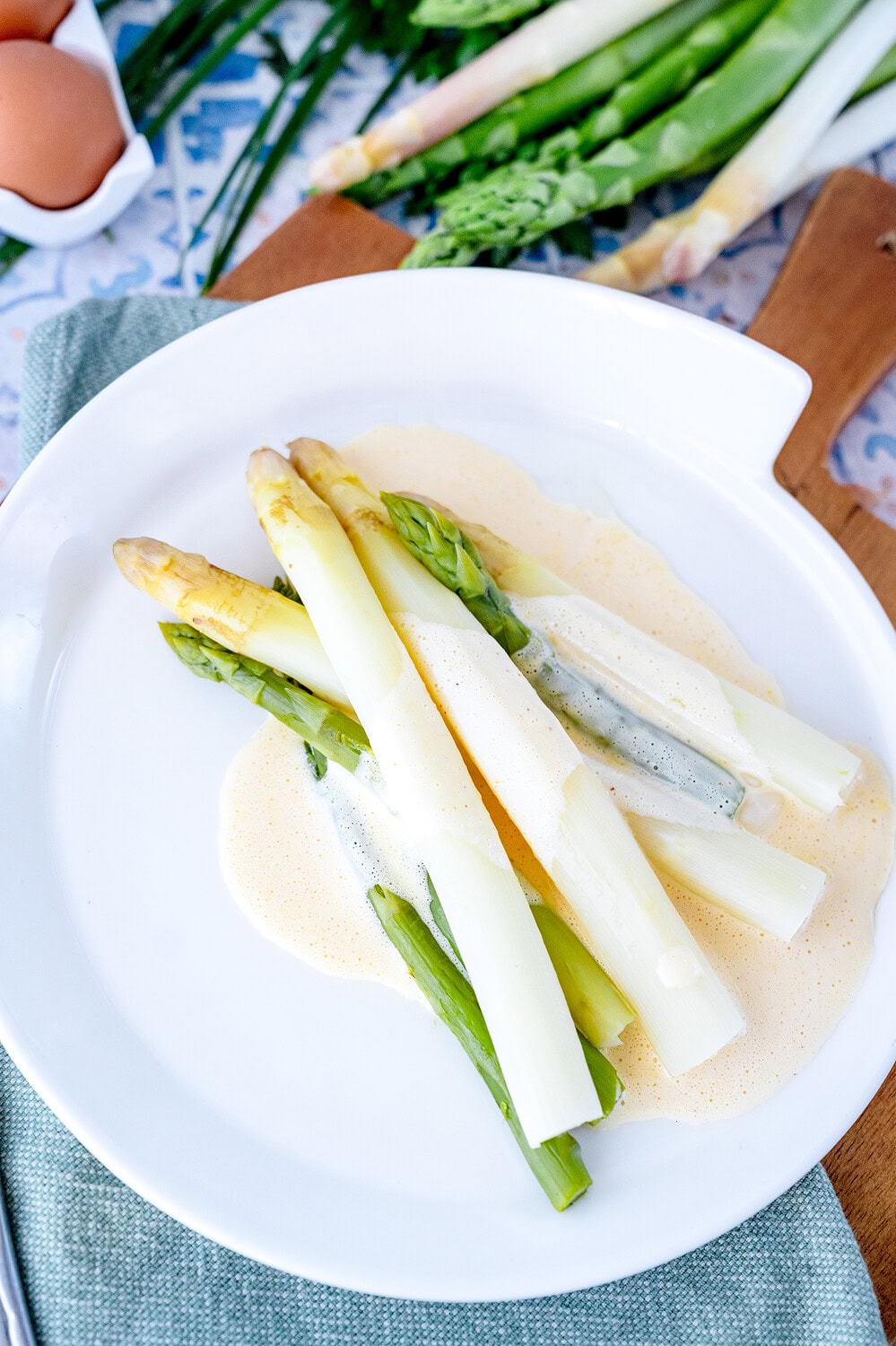 White plate with green and white cooked asparagus and flash hollandaise