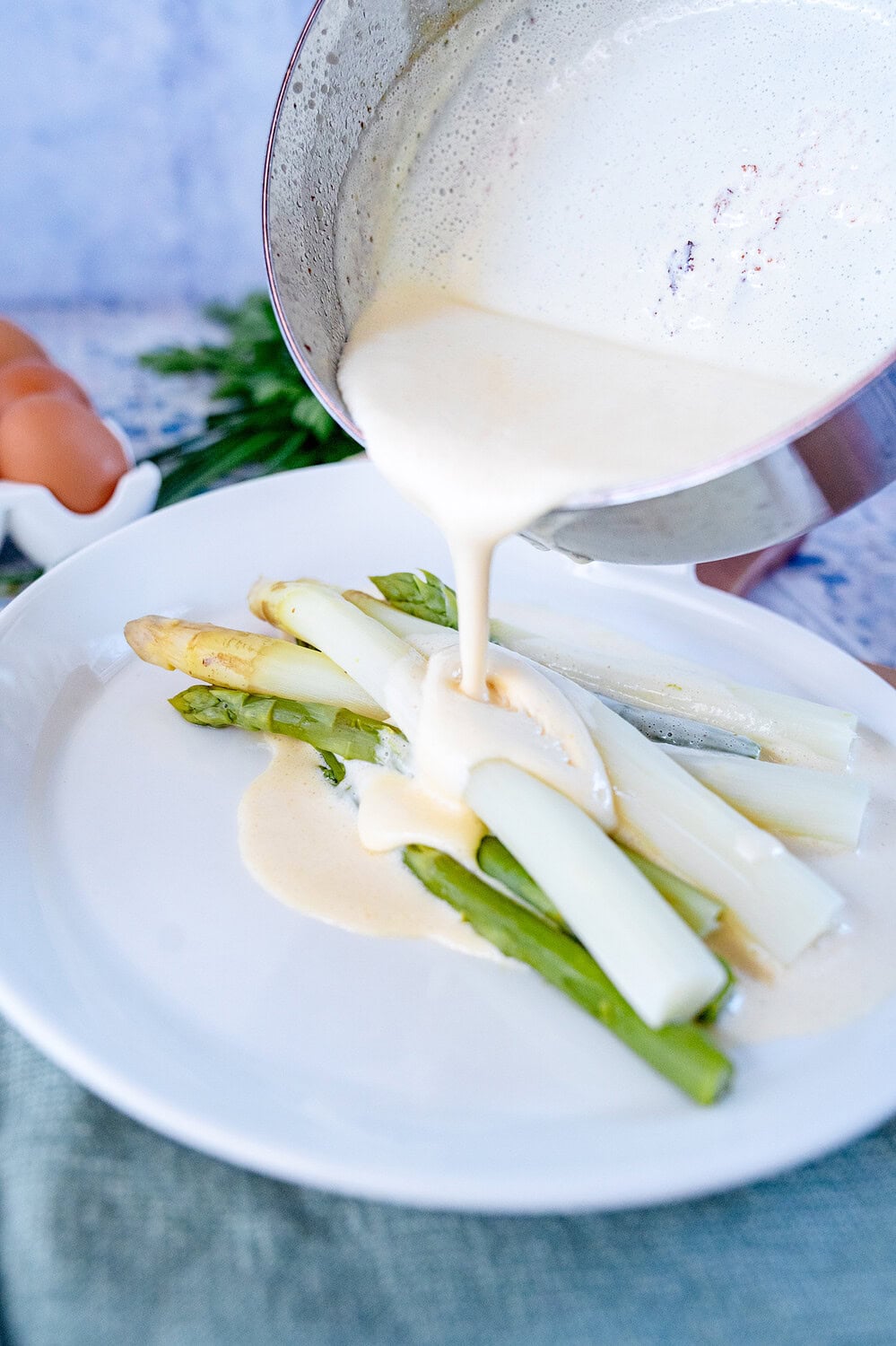 Blitz hollandaise being poured from a pot onto the plate with green and white asparagus.