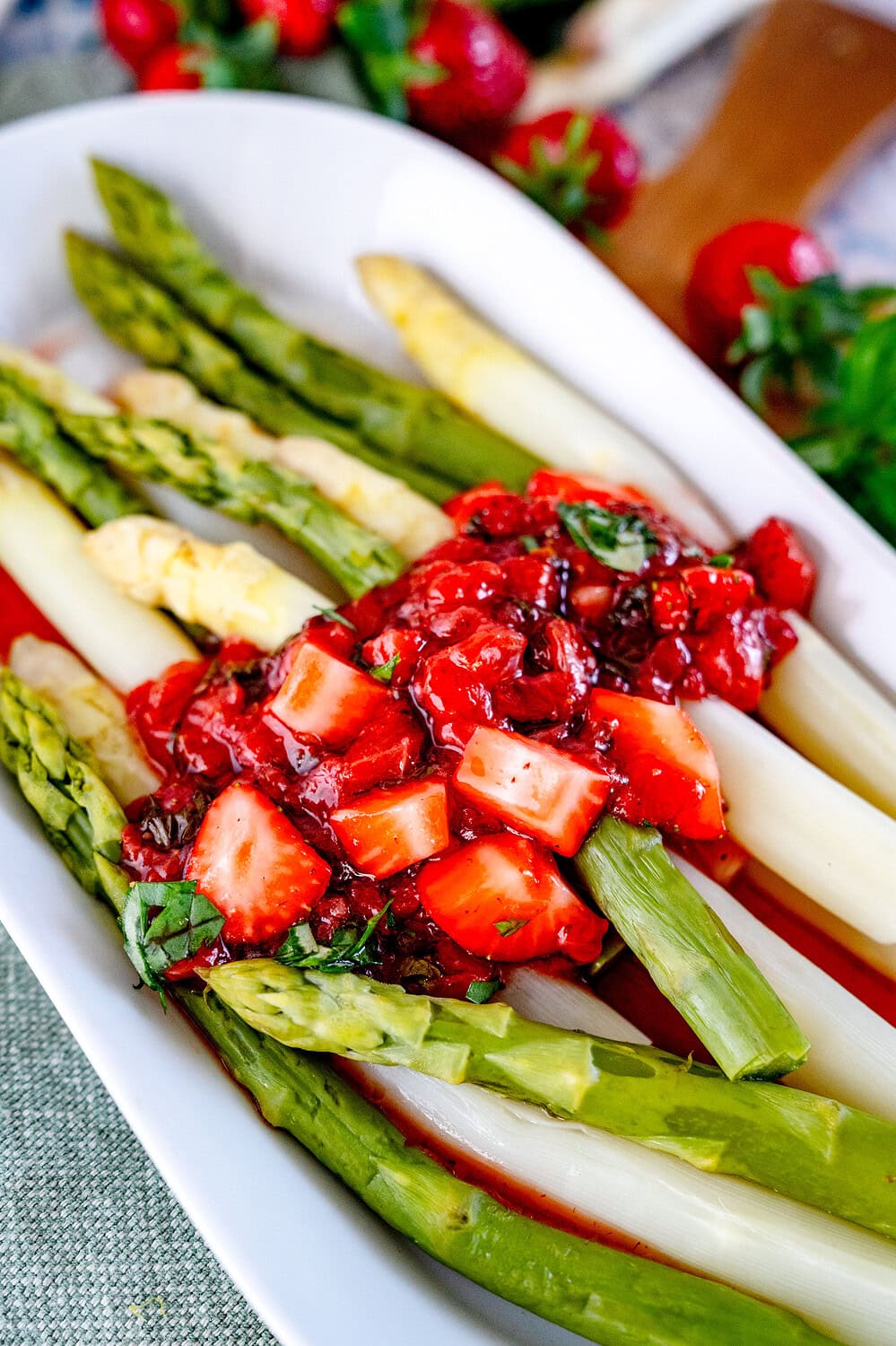 Close-up of an oblong plate with green and white asparagus. A red strawberry chutney is spread on top