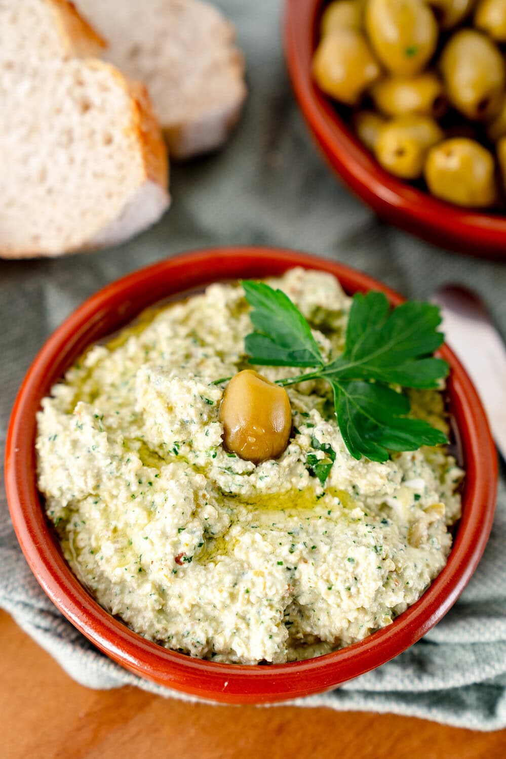 Grüner Olivendip mit einem Blatt Petersilie und Baguette in einer Tonschale