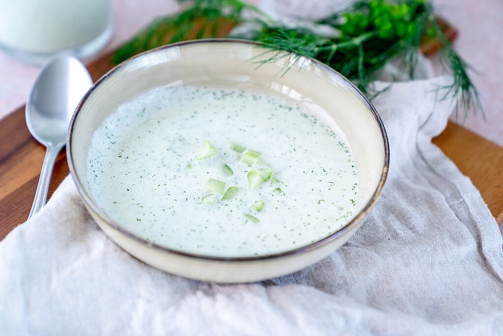 A soup plate with fresh cold cucumber soup and dill in the background