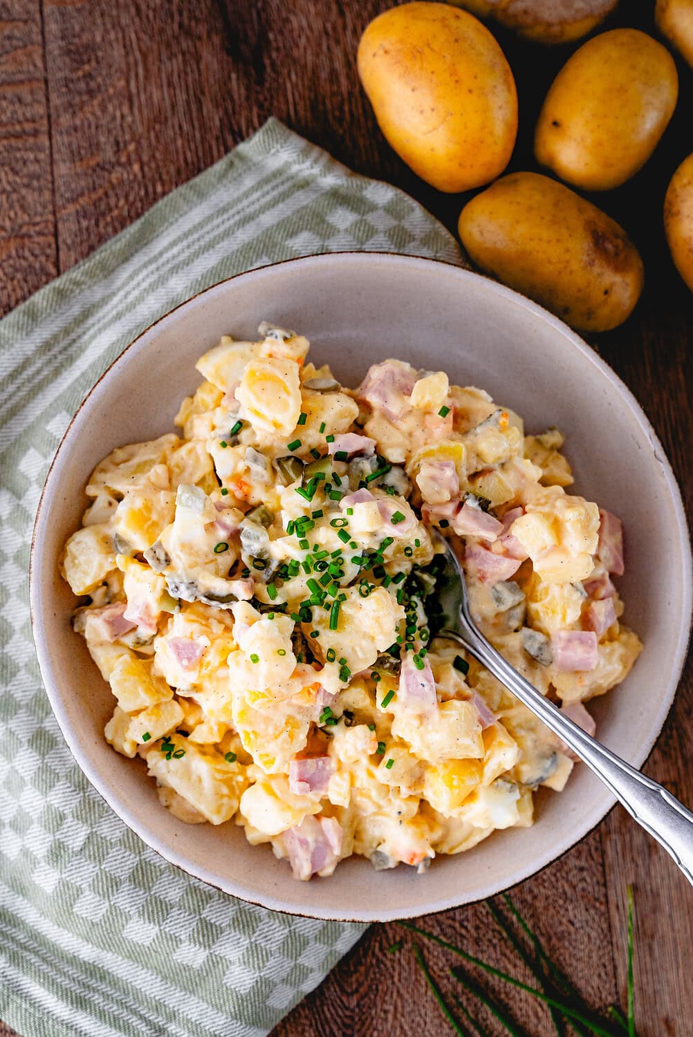 Potato salad with ham sausage and chives on a wooden board with a green cloth