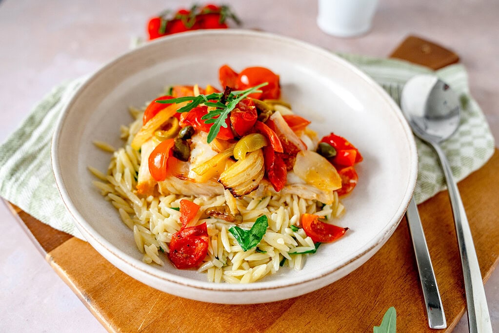 Toskanischer Fisch aus der Heißluftfritteuse mit Kirschtomaten und Nudeln auf einem Teller, der auf einem Holzbrett steht