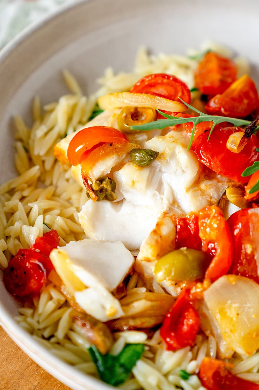 Zerzupfter weißer Fisch mit Kirschtomaten auf einem Teller mit Nudeln und Rucola
