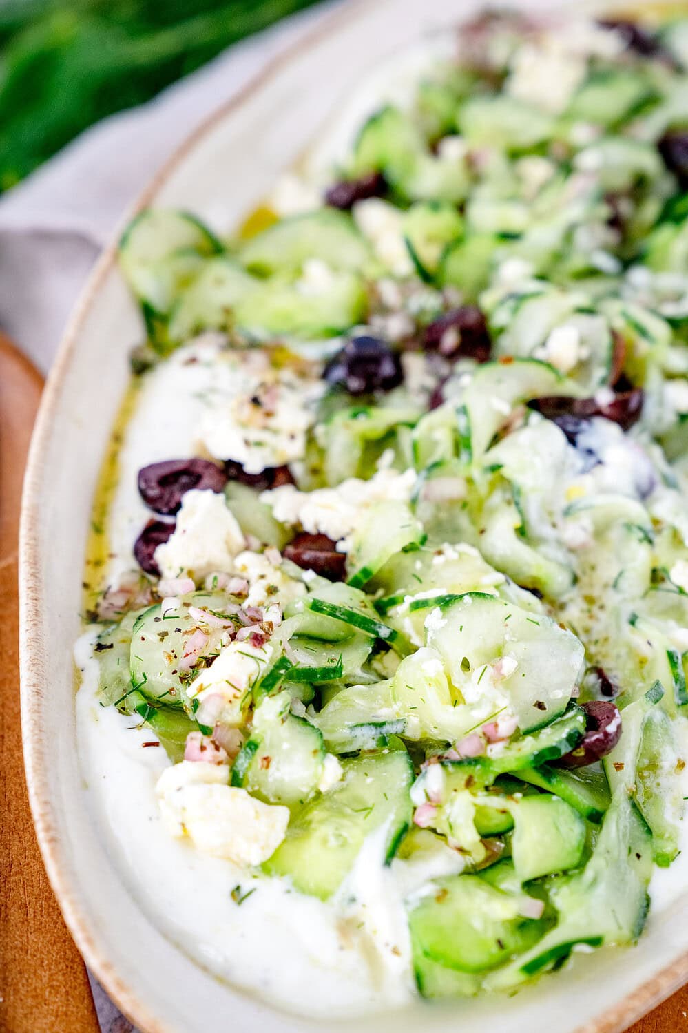 Nahaufnahme des griechischen Gurkensalates. Man sieht den Rand der Form auf dem Boden der Fetacreme ist dann die Gurkenscheiben, Zwiebeln, Oliven und Gewürze vom Dressing
