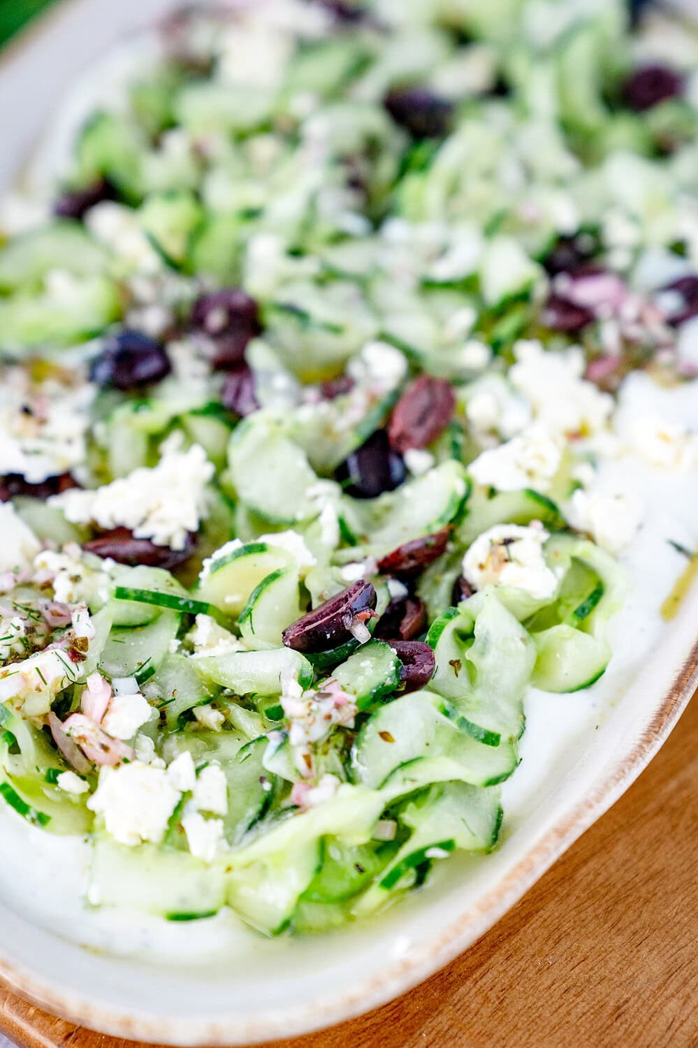 Nahaufnahme des griechischen Gurkensalates. Die Gurke ist spiralförmig geschnitten worden und liegt auf der Fetacreme und ist mit Oliven und Feta bedeckt