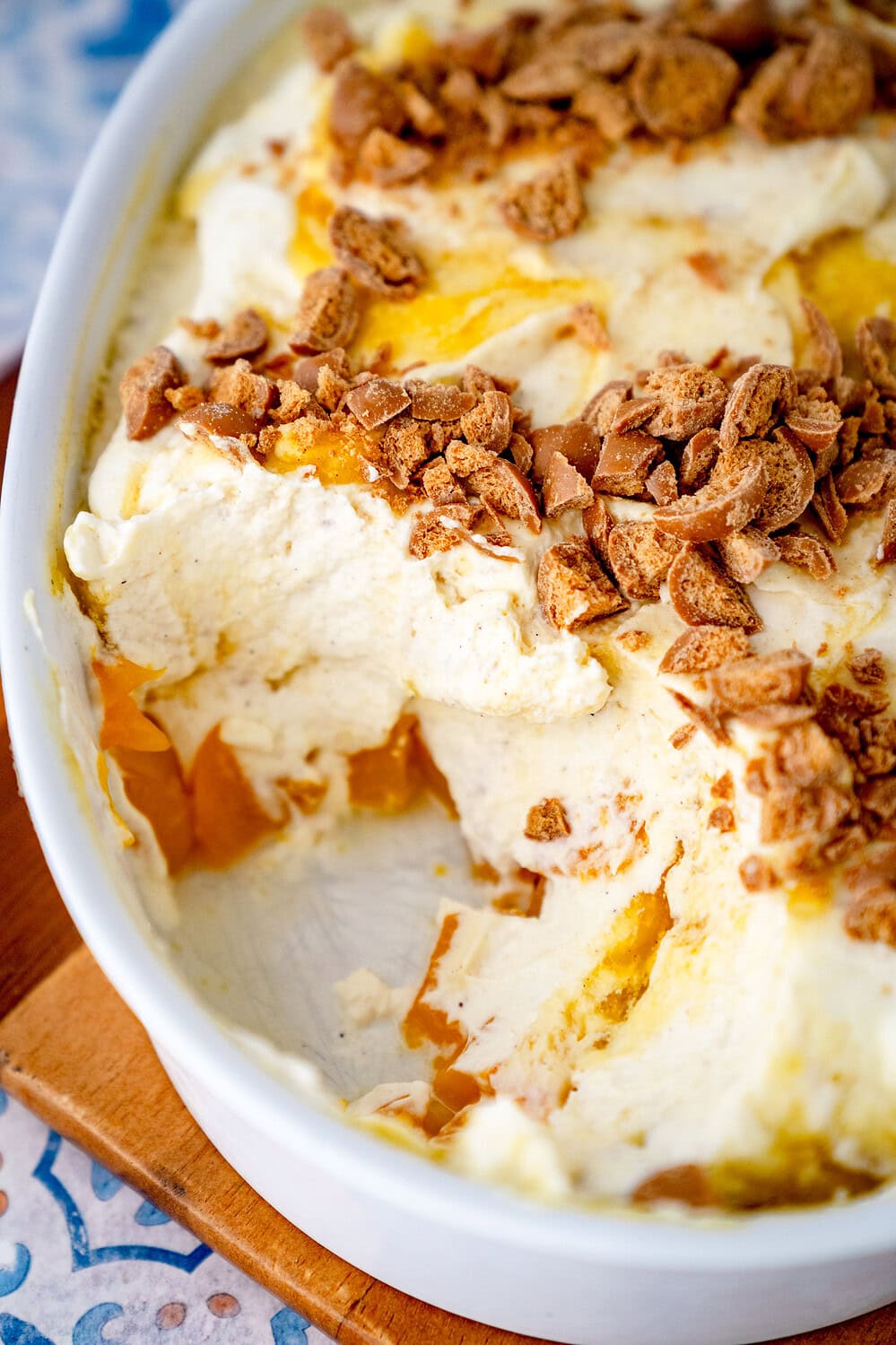 Solero dessert with passion fruit quark in a baking dish from which a piece has already been removed. You can see diced peaches in the bottom layer, followed by a cream quark cream with yellow sauce and biscuit crumbs.
