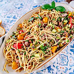 Spaghettisalat mit Salami und Mozzarella in einer Servierschale mit Salatbesteck daneben