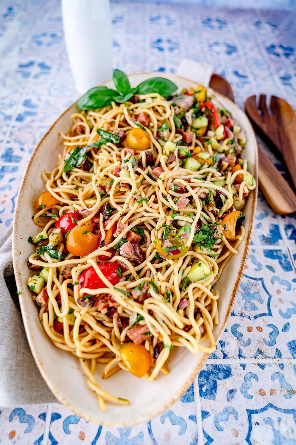 Spaghettisalat in einer Servierschüssel mit Salamiwürfeln, bunten Tomaten und kleingeschnittenem Basilikum