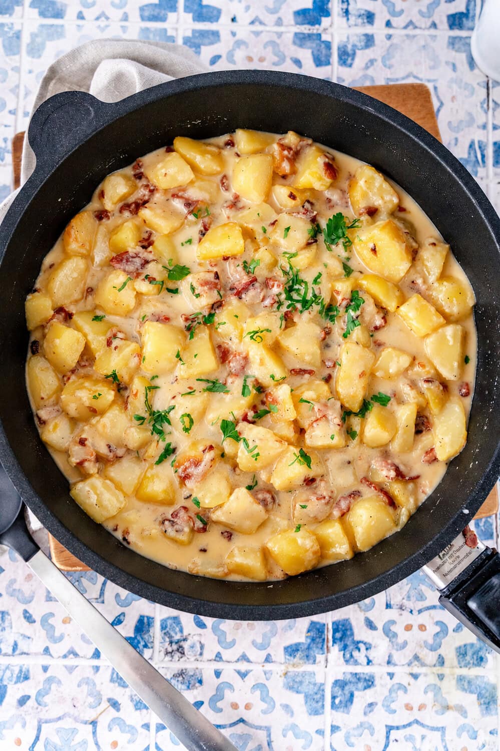 Kartoffel-Carbonara-PFanne Draufsicht auf den Mann, der die Kartoffelwürfel, cremige Sauce und Speck in der Pfanne sieht. Es ist mit Petersilie bestreut.