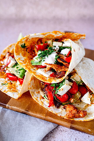 Drei Hähnchen-Fajitas aus dem Airfryer liegen auf einem Holzbrett mit der Öffnung zu einem